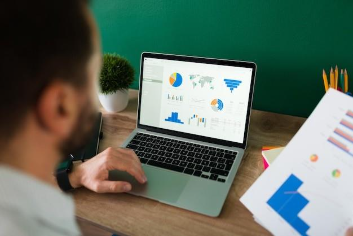 rear view of a young man working on his laptop and looking at a work report and graphs